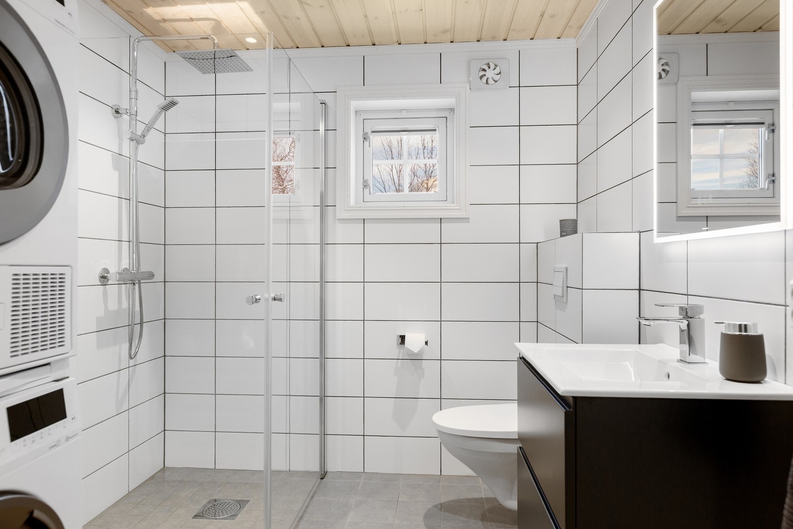 Bad/vaskerom med baderomsinnredning, vegghengt toalett, dusj med glassdører og opplegg for vaskemaskin. Galleribilde