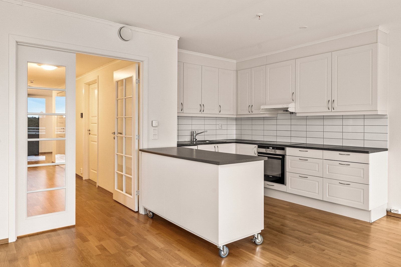 Innredningen er lys med profilerte fronter og laminert benkeplate, kombinert med kitchenboard-plater mellom benk og overskap for et praktisk og lettstelt uttrykk. Galleribilde