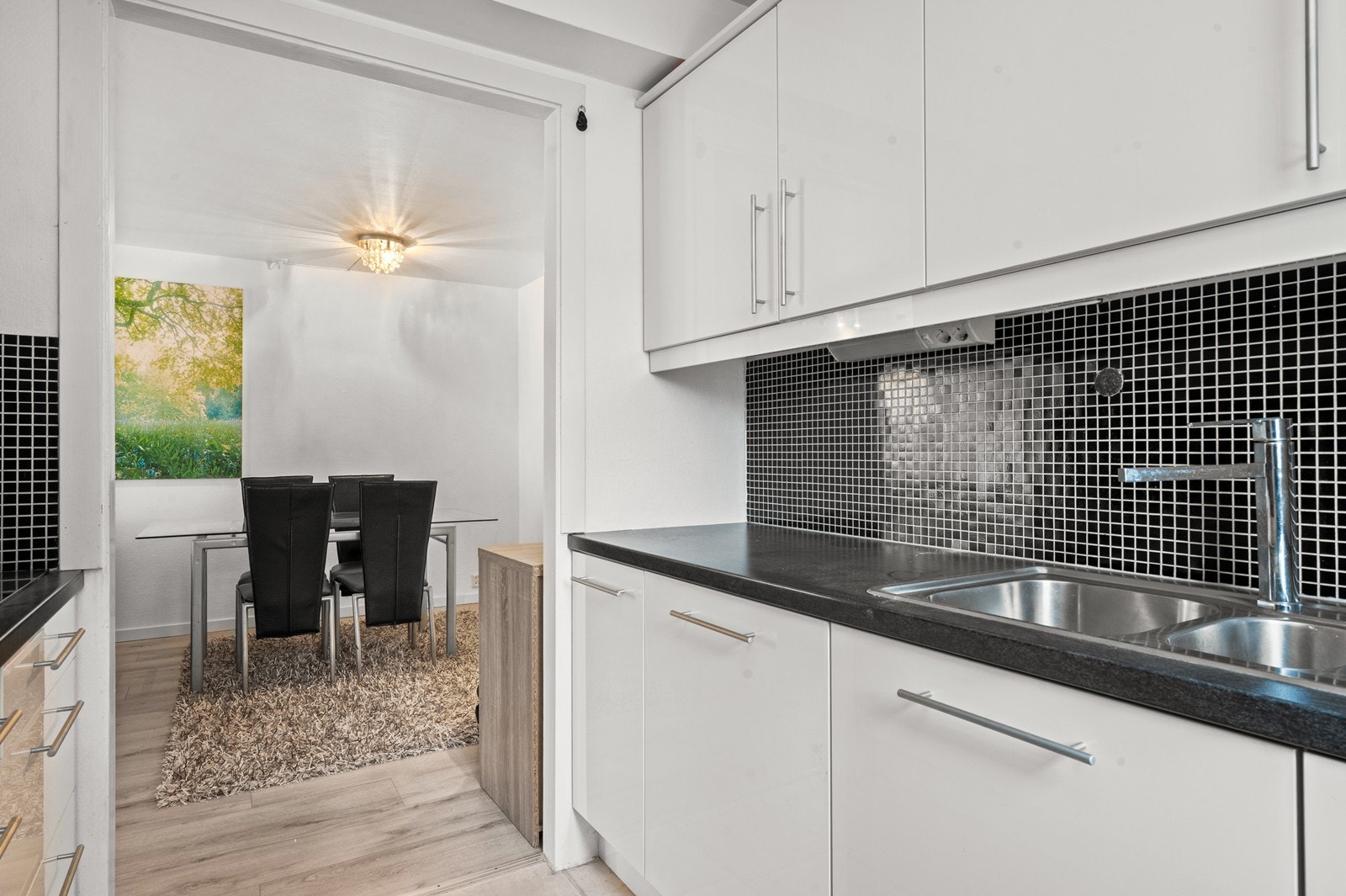 Kjøkkenet har en praktisk utforming. Her er det belegg på gulvet, vegger og himling har de samme slette overflatene som øvrige deler av boligen. Det er fliser mellom benk o overskap i en mørkere kontrastfarge. Galleribilde