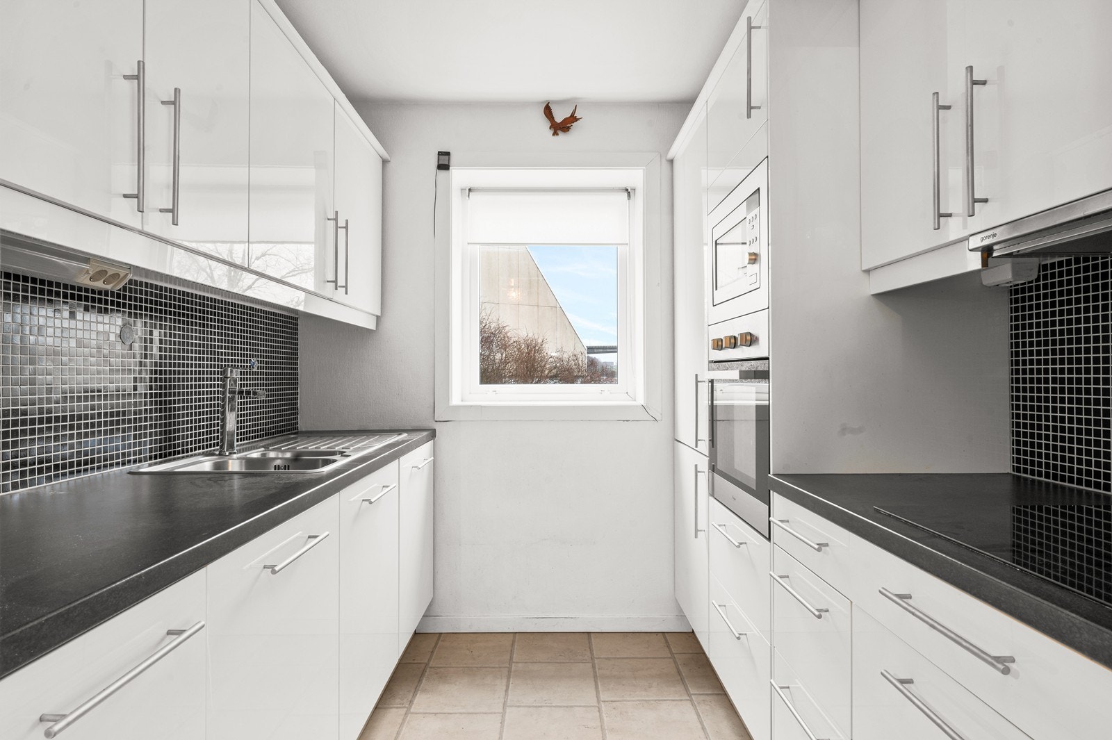 Innredningen er moderne, med slette, hvite fronter i høyglans, laminat benkeplate og integrerte hvitevarer. Det er montert ventilator med kullfilter over koketoppen. Galleribilde