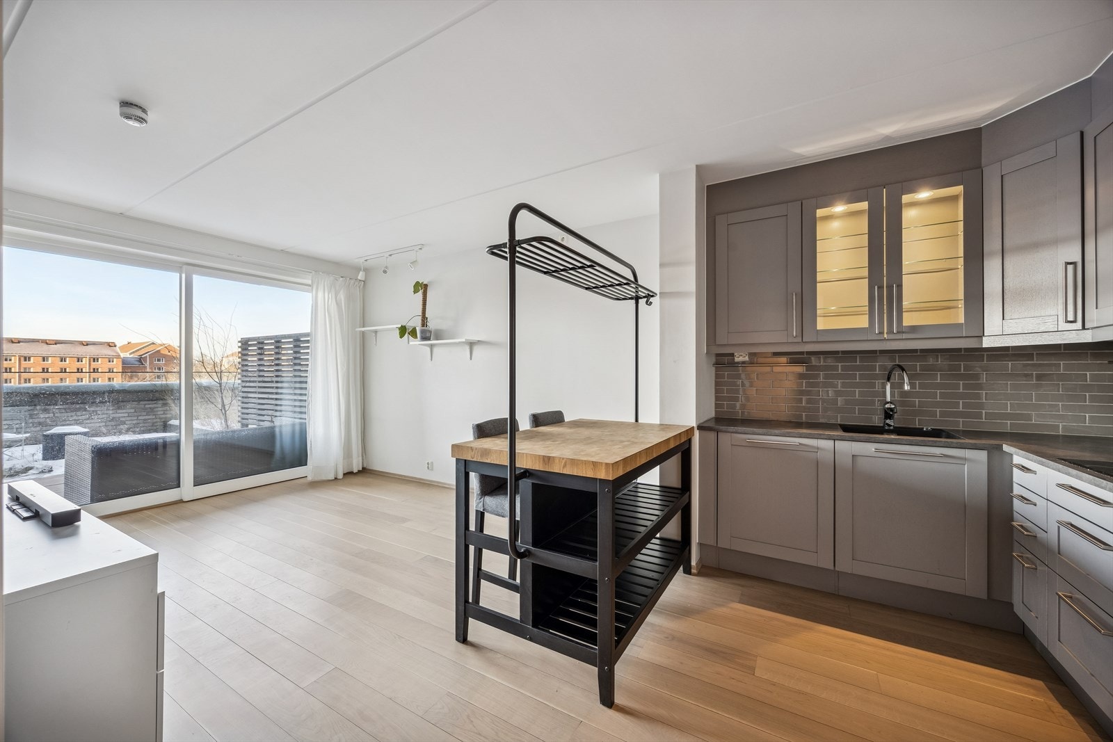 Kjøkkeninnredning fra Sigdal med integrerte hvitevarer og grå profilerte fronter. Integrerte hvitevarer samt kjøkkenøy med barstoler medfølger. Galleribilde