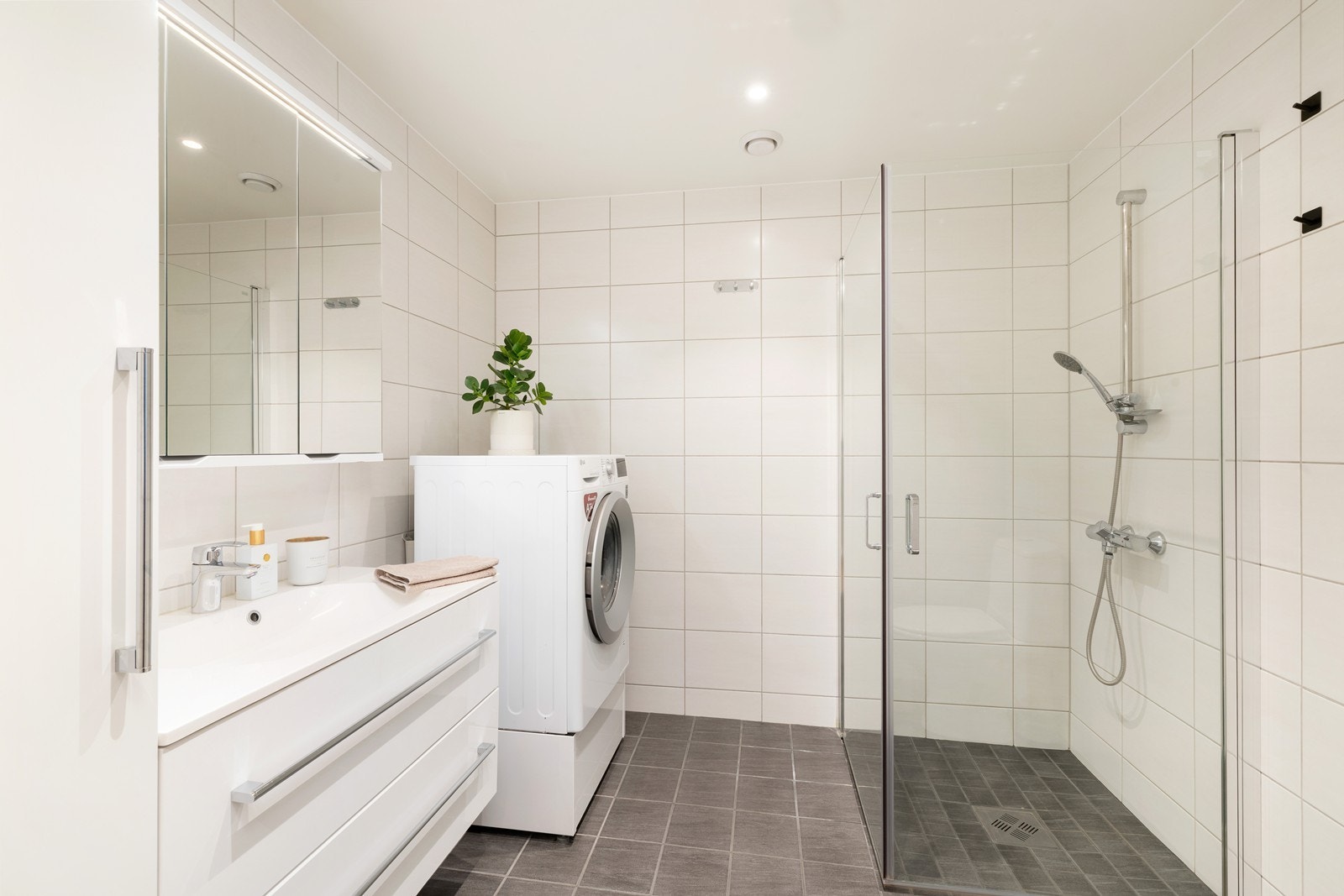 Flislagt bad utstyrt med dusj, servant med skap, varme i gulv, toalett og opplegg for vaskemaskin Galleribilde