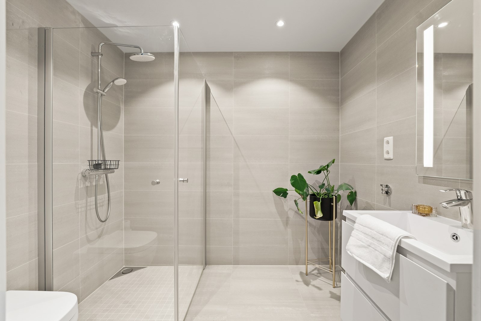 Lekkert baderom med gulvvarme. Rommet er innredet med vegghengt toalett, tidløs baderomsinnredning og dusjhjørne med regnfallsdusj. Galleribilde