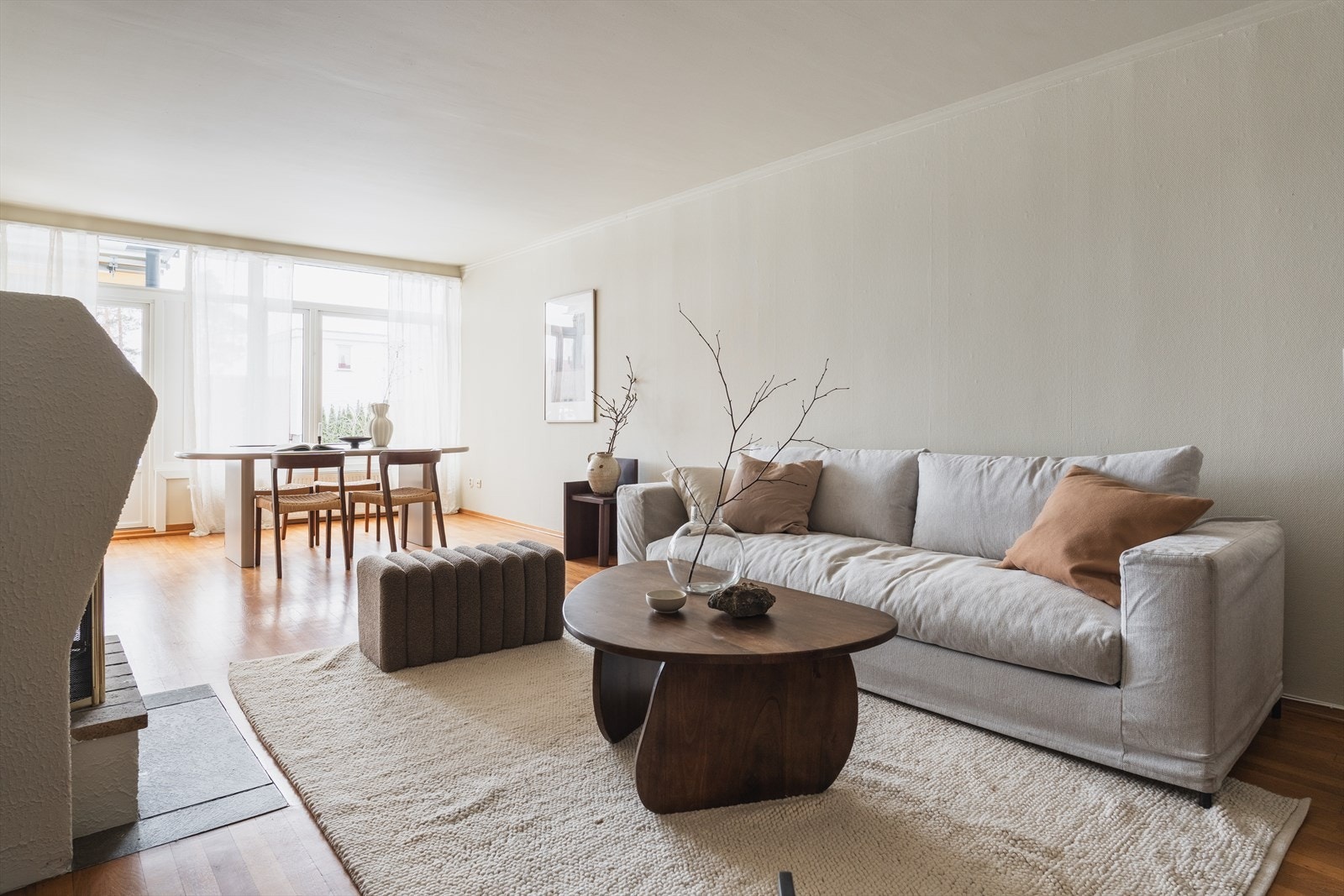 Åpen stue med peis, sofagruppe og spiseplass samlet i ett. Store vindusflater med lette gardiner slipper inn mye dagslys. Galleribilde