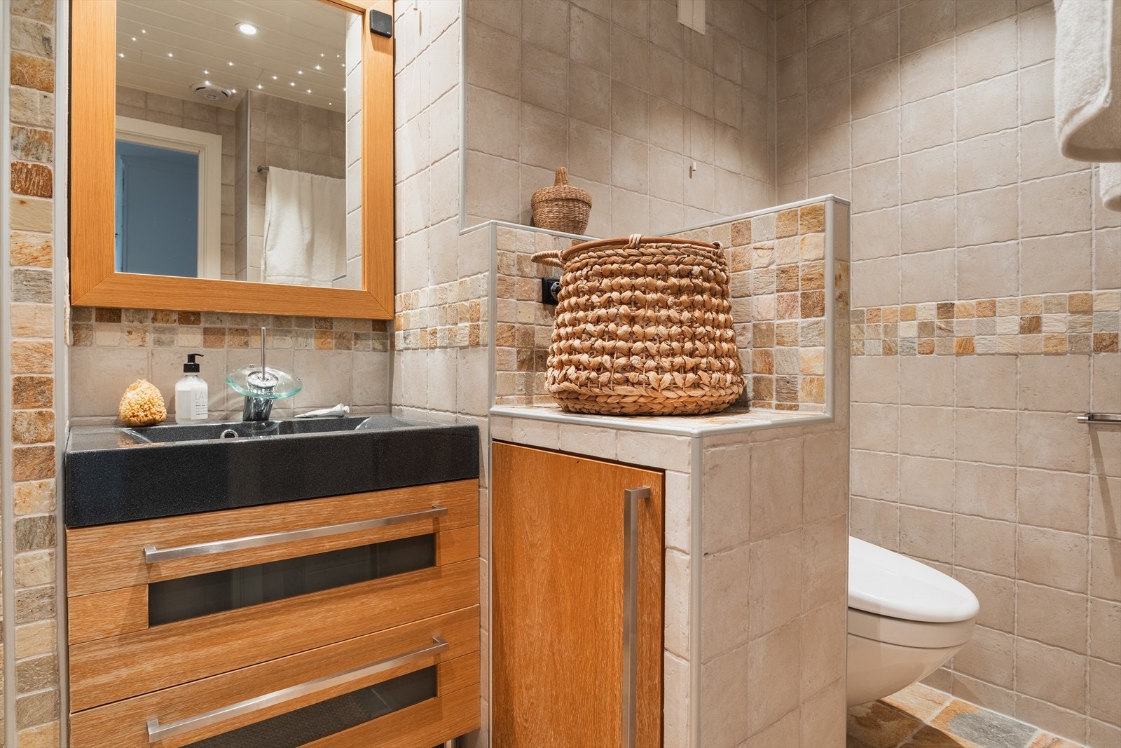 Flislagt bad fra 2007 i varme naturtoner med praktisk innredning og god oppbevaringsplass. Servant i mørk stein gir en eksklusiv kontrast, mens speil og behagelig belysning skaper en lun og innbydende atmosfære. Galleribilde