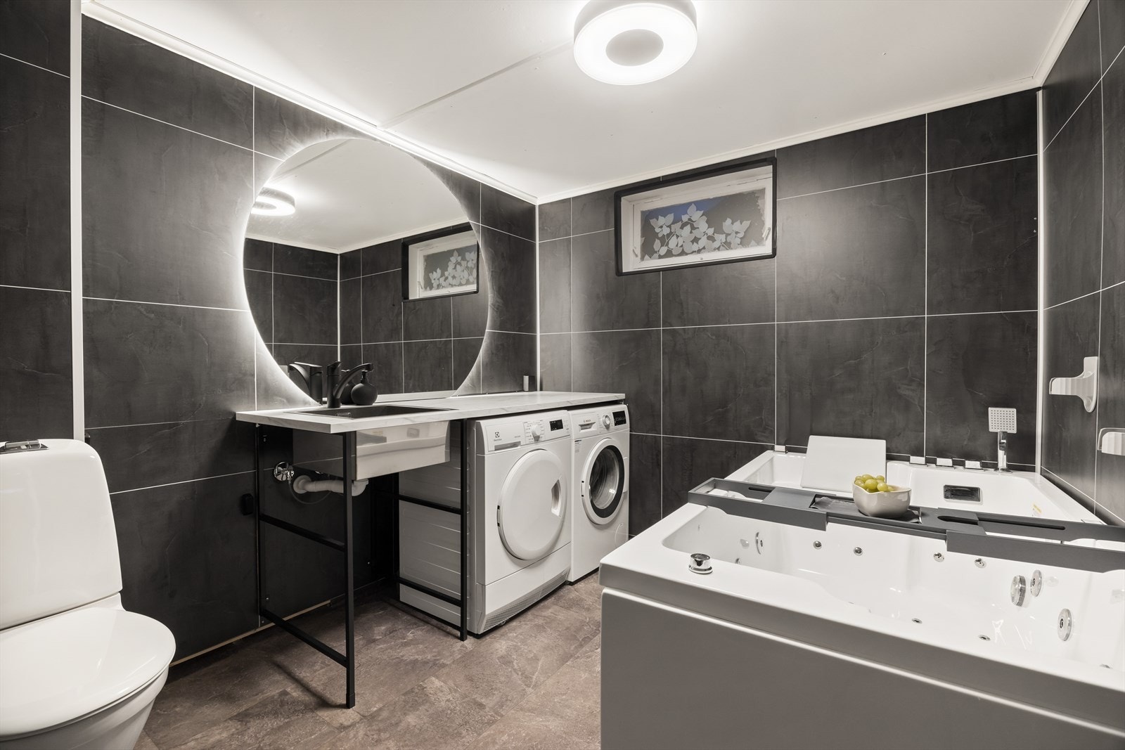 Kombinert bad og vaskerom i underetasjen. Det ble i 2024 lagt nytt vinylbelegg på gulv samt nye våtromsplater på vegger. Vinylbelegget er lagt over tidligere monterte varmekabler i gulv. Det er etablert nytt sluk, klemt i vinyl mot opprinnelig avløp/sluk. Galleribilde