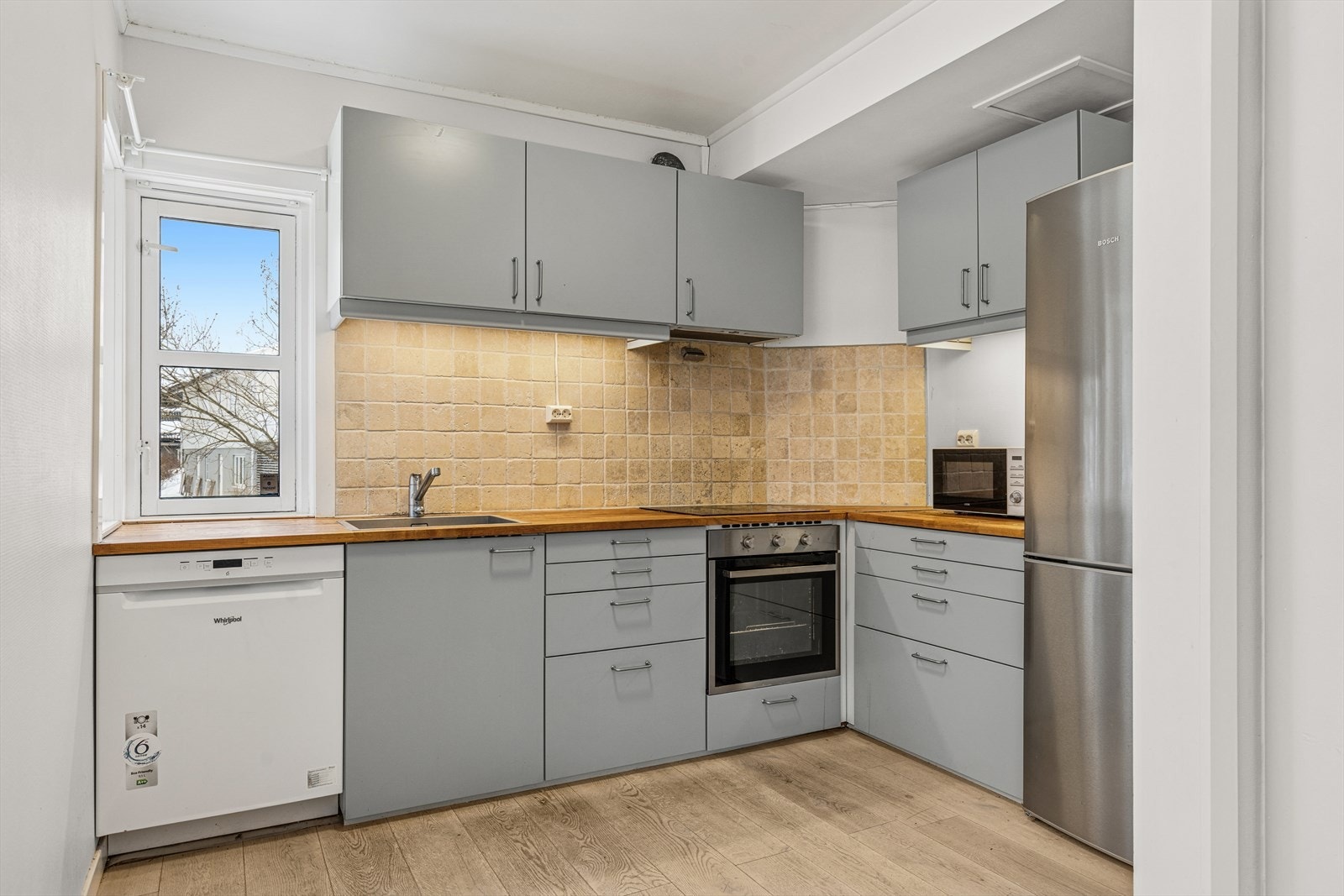 Kjøkken med glatte fronter, fliser på vegg over benkeplaten i heltre. Her er det opplegg for oppvaskmaskin og montert komfyrvakt. Galleribilde