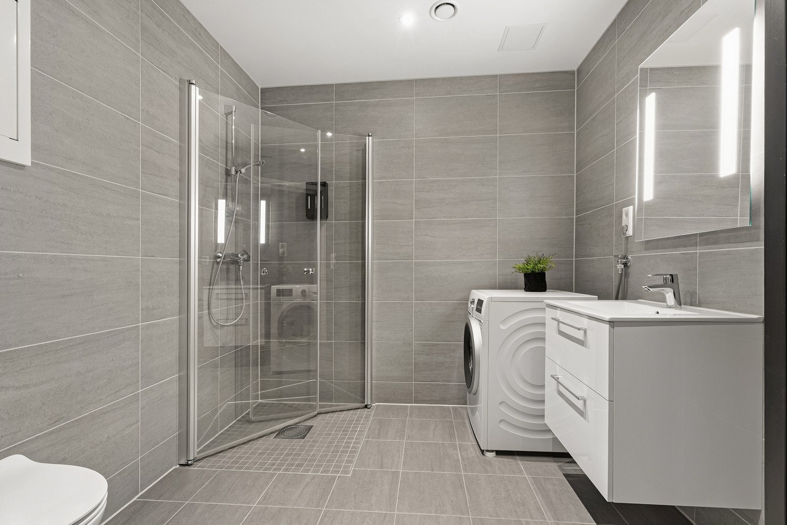 Stilrent og moderne bad med grå fliser, varmekabler i gulv og en utstrakt bruk av downlights i himling. Galleribilde