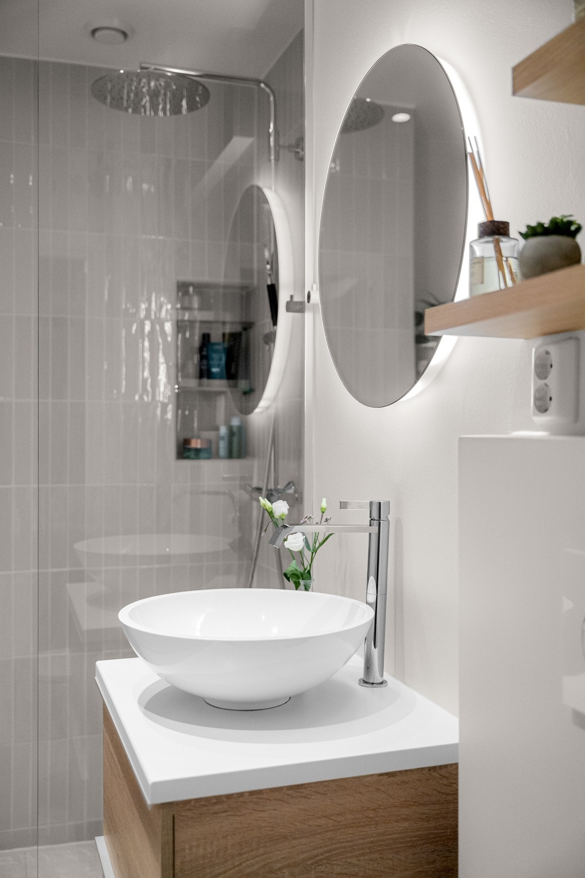 Flott baderomsinnredning med skuffer og lys benkeplate med ovenpåliggende bolleservant, rundt speil med integrert belysning over. Galleribilde