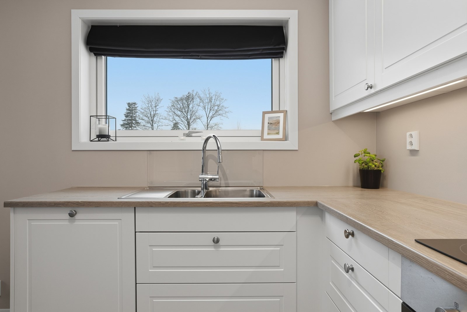 Lyst og moderne kjøkken med praktisk planløsning, stort vindu, og god benkeplass. Galleribilde