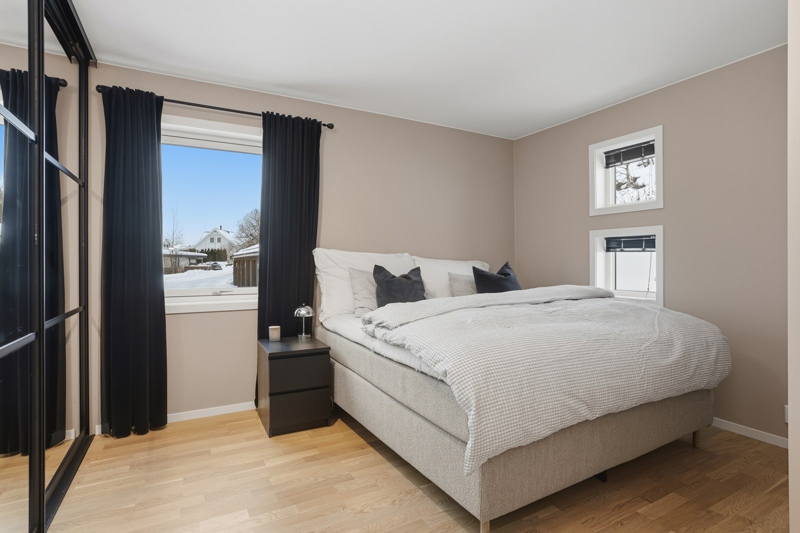 Sjarmerende soverom med nøytral fargepalett og naturlig lysinnslipp. Stort vindu med utsikt mot idyllisk, vinterkledd nabolag. Galleribilde