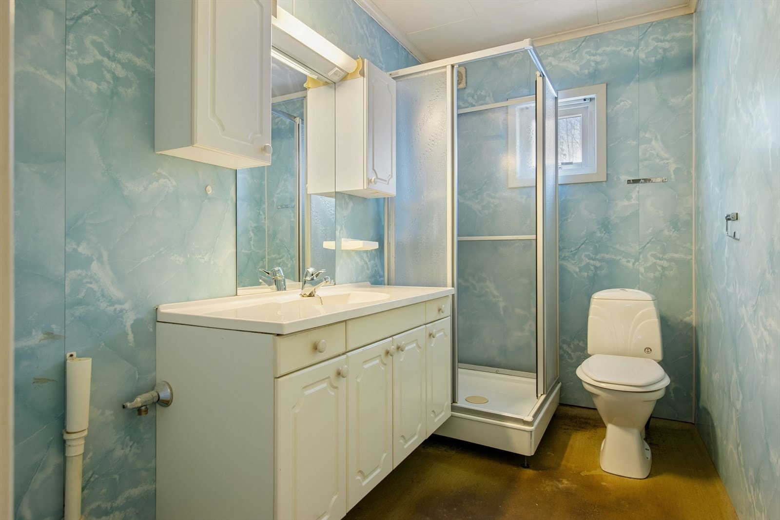 Kombinert bad/vaskerom med servant med underskap, speil, gulvmontert toalett, dusjkabinett og opplegg for vaskemaskin. Galleribilde