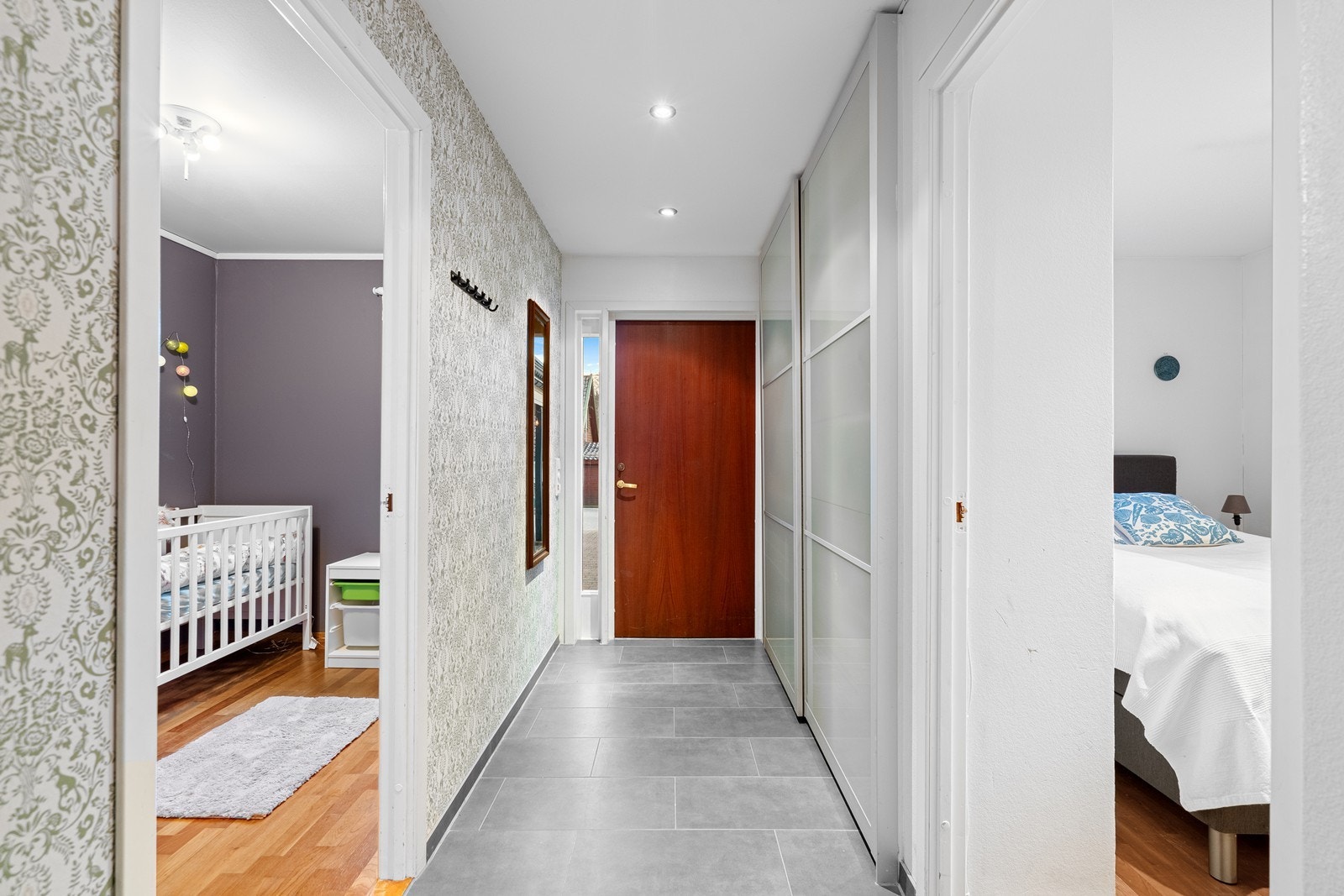 Velkommen inn. Entre med fliser på gulv og skyvedørsgarderobe for oppbevaring av klær og sko. Galleribilde