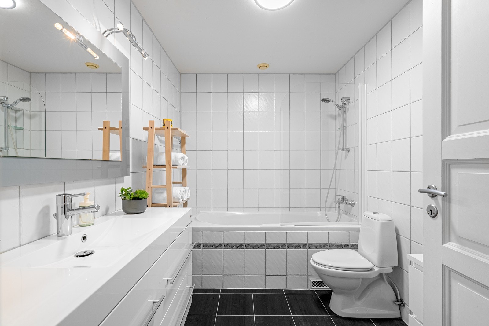 Flisebelagt bad er innredet med vask i seksjon, toalett og kar med dusj. Galleribilde