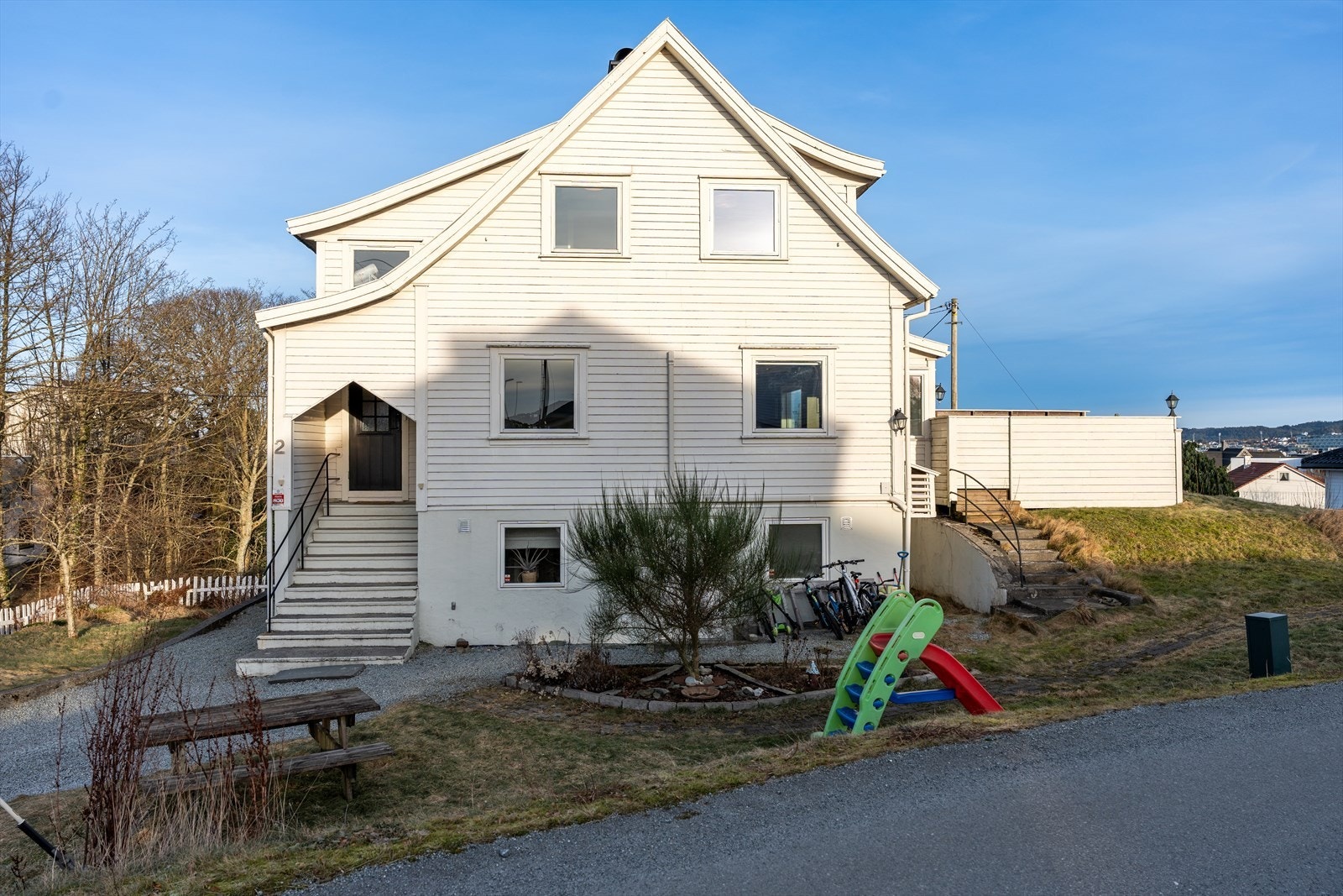 Eiendommen har singel i gårdsrom, ellers noe kupert, beplantet med trær, plen, busker og bed Galleribilde