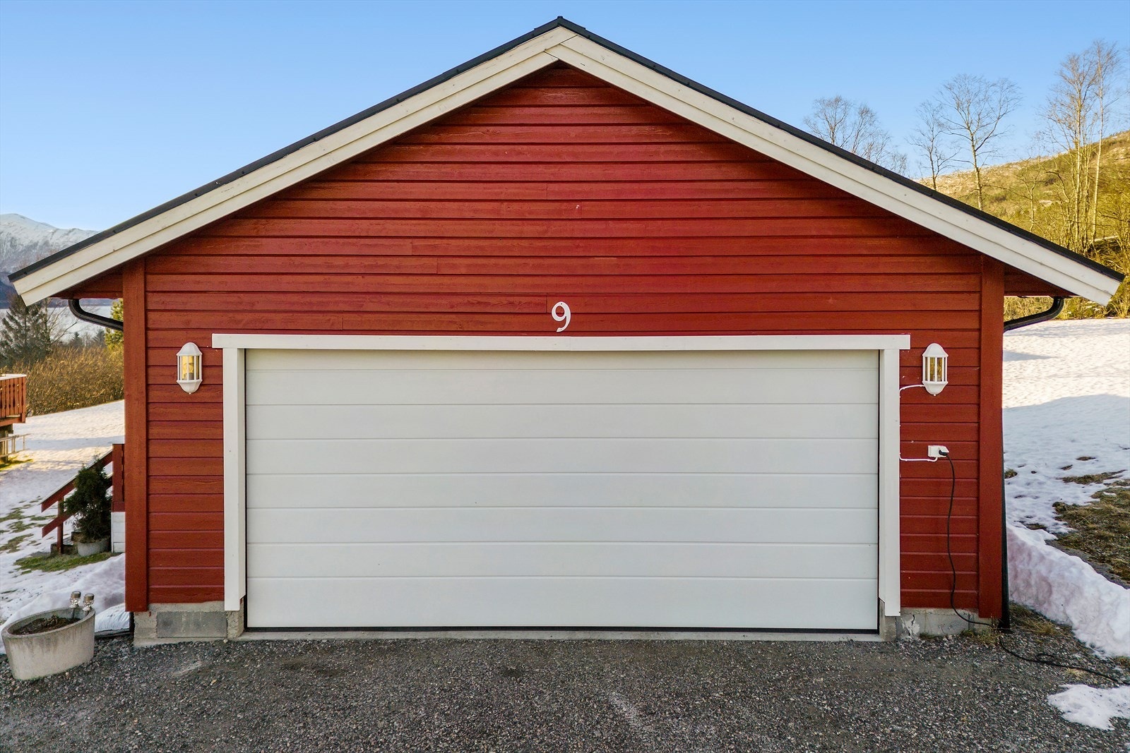Garasjen har en stor leddet aluminiumsport med portåpner og er oppført med liggende bordkledning. Galleribilde