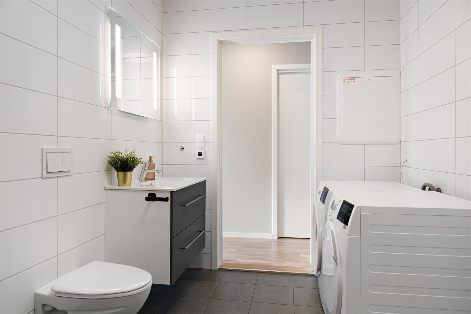 Det inneholder vegghengt toalett, dusj med innfellbare glassdører, servant med underskap og opplegg for vaskemaskin. Her er også varmtvannsberederen plassert. Galleribilde