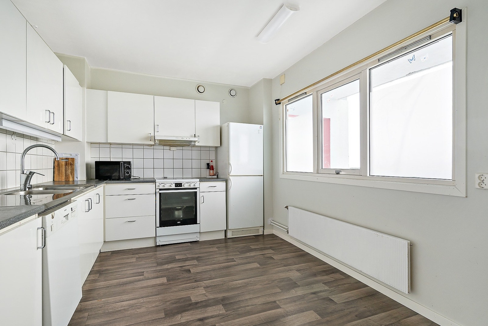 Lyst kjøkken med glatte fronter, laminat benkeplate og nedfelt stålkum. Innredningen har nisjer til komfyr, oppvaskmaskin og kjøleskap. Galleribilde