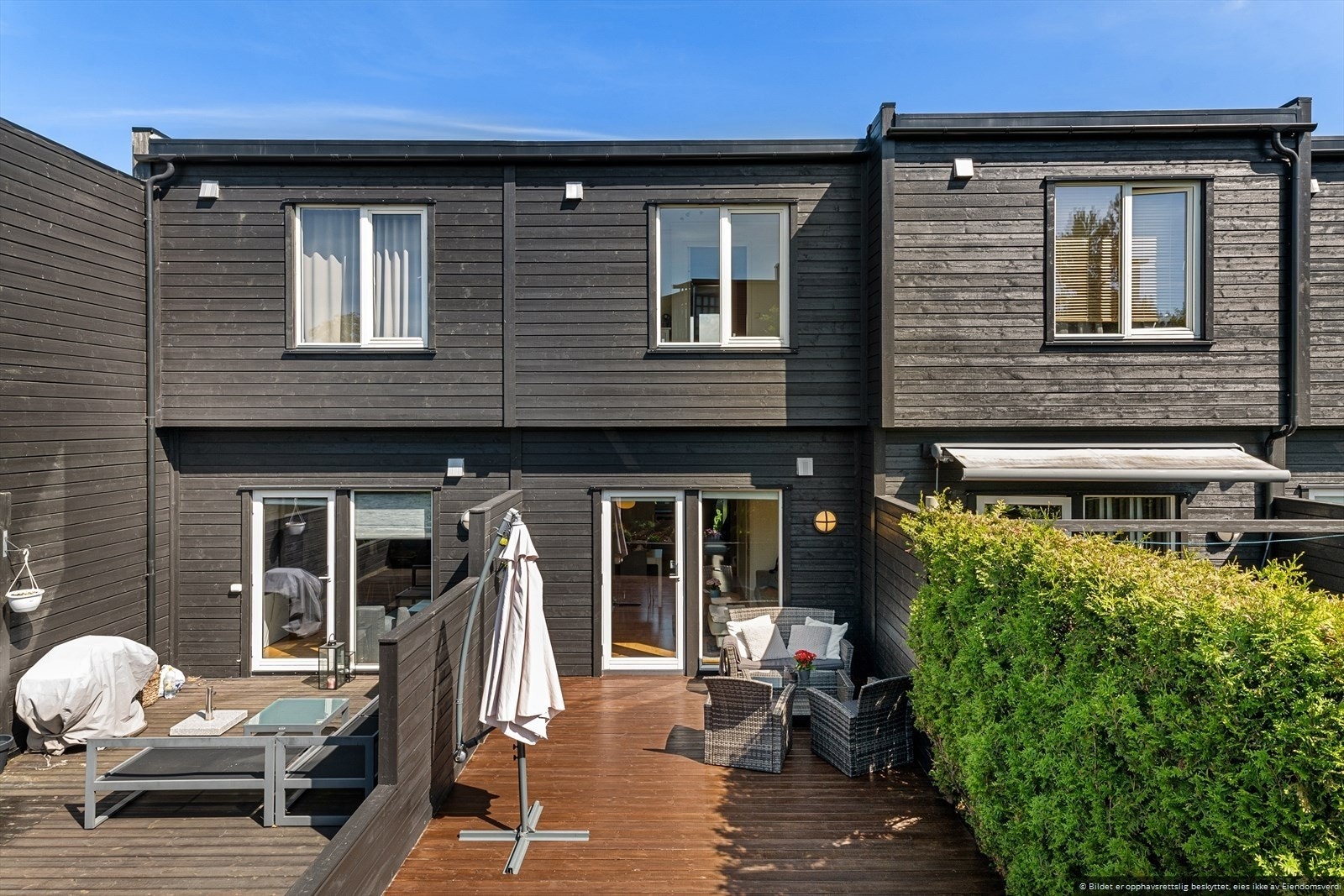 Terrasse/platting på bakke og grøntareal beplantet med plen, bed og busker. Galleribilde