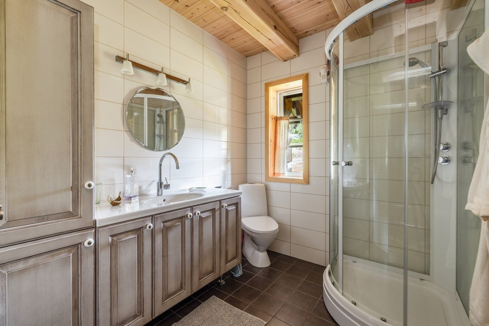 Lyst, flislagt bad med varmekabler, toalett og dusjkabinett, samt romslig servantskap med heldekkende servantplate og høyskap. Galleribilde