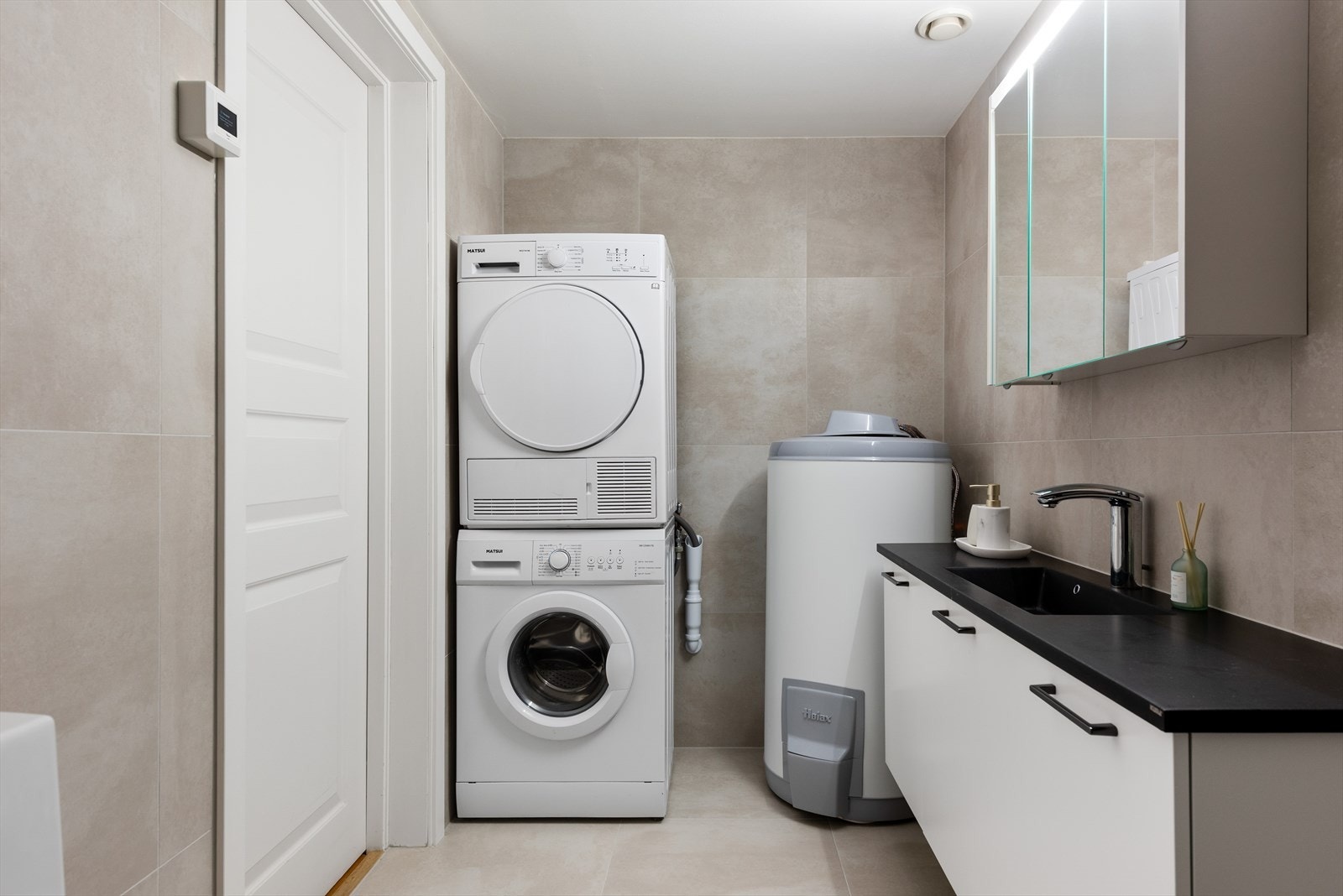 Meget pent baderom med gulvvarme, fliser, innredning, stor bereder og opplegg for vaskemaskiner. Galleribilde