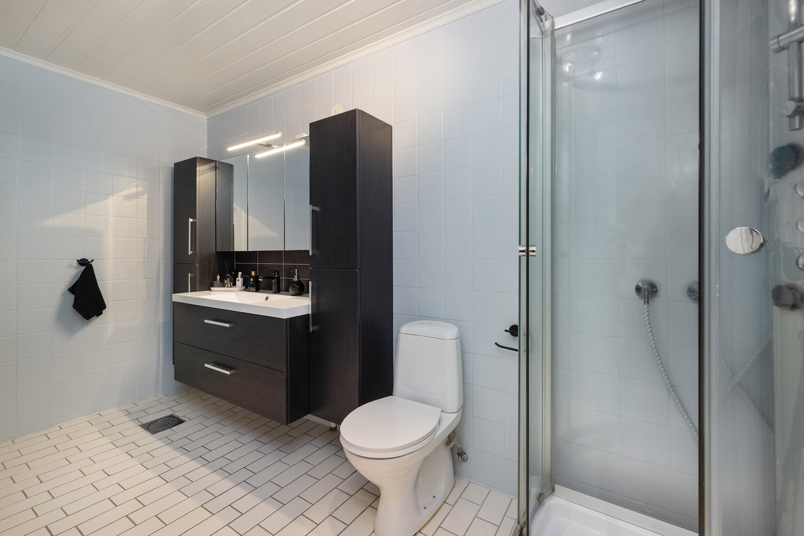 Helfliset bad i underetasjen med mørk baderomsinnredning og dusjkabinett. Galleribilde