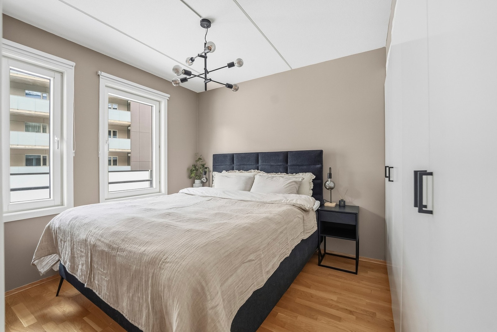 Lyst og tiltalende soverom med malte slette veggflater, parkett på gulv og to store vinduer som slipper inn godt med lys. Galleribilde