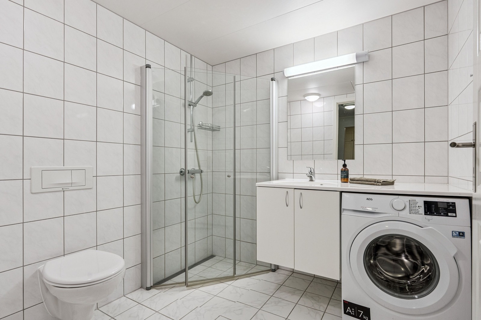 Hovedbad med vegghengt toalett, dusjsone og innredning med plass for vaskemaskin. Galleribilde