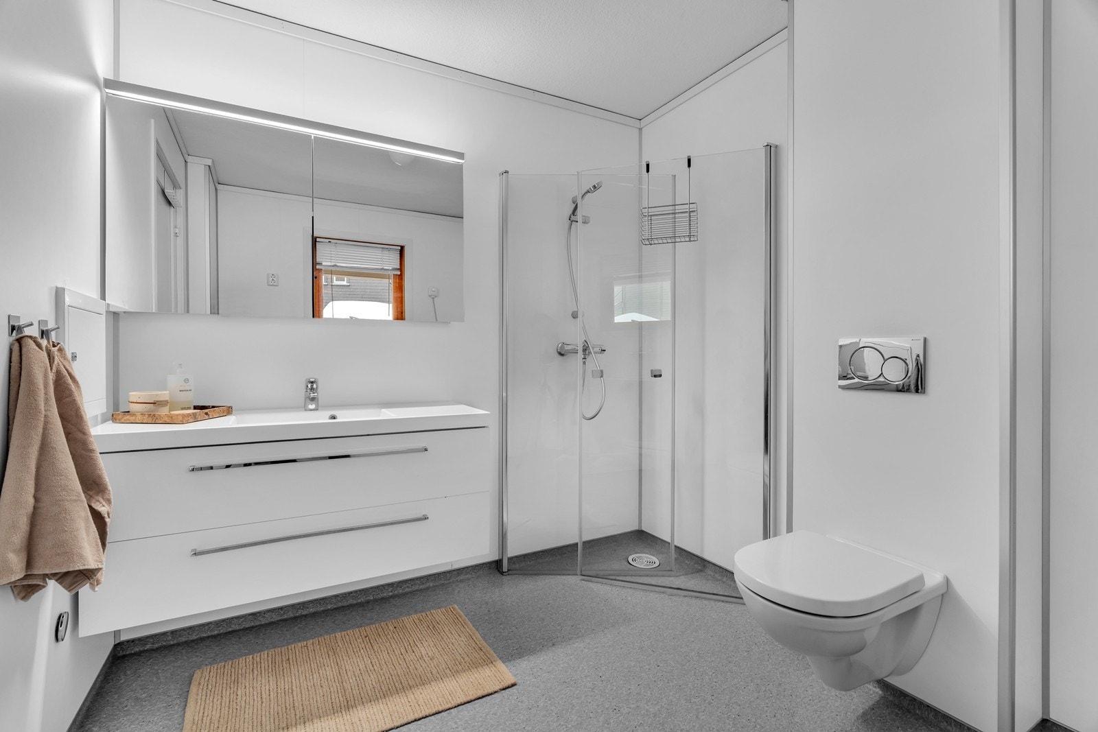 Romslig baderom med vegghengt toalett, baderomsinnredning og dusjhjørne med innfellbare dusjdører Galleribilde