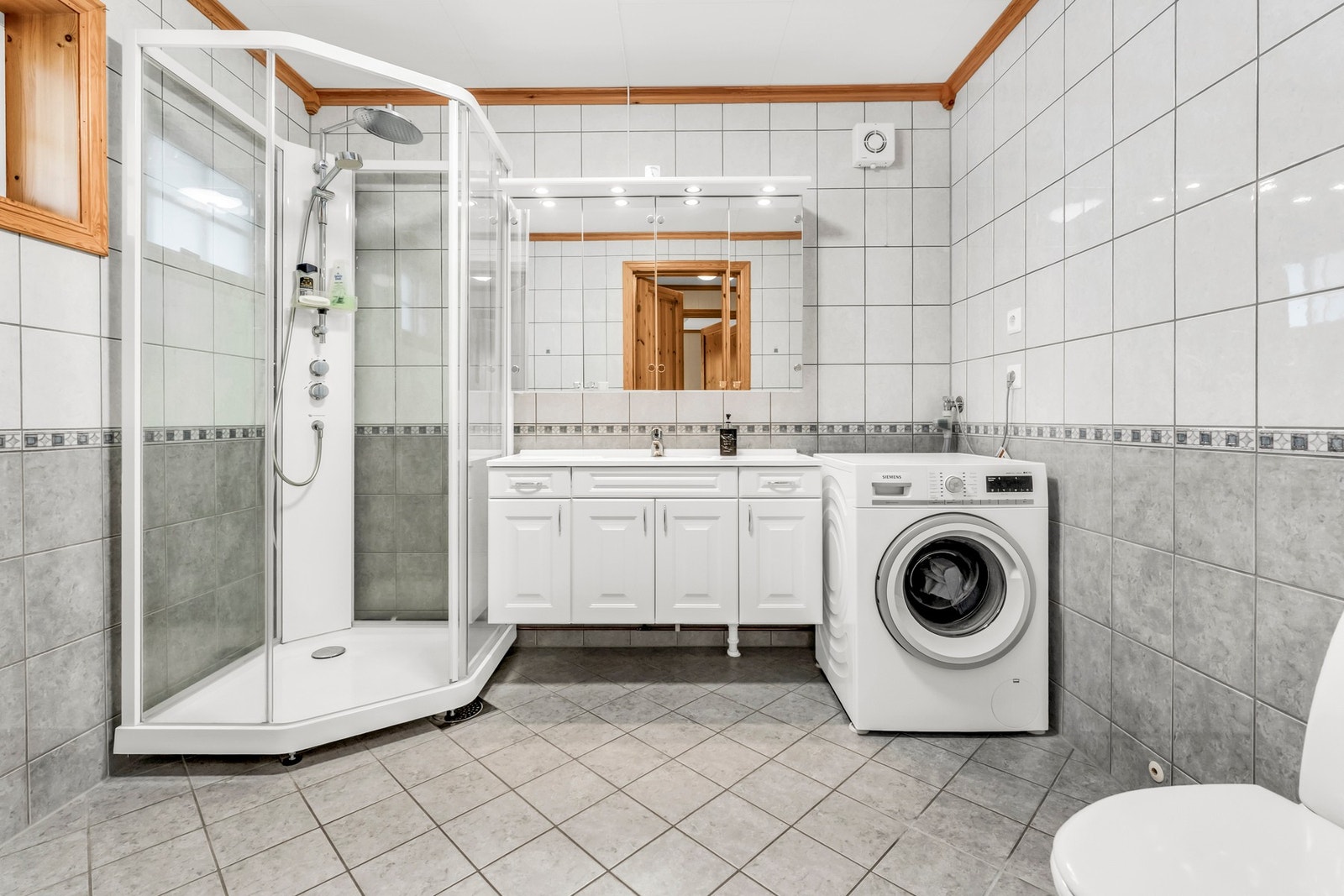 Romslig flislagt bad med elektriske varmekabler i gulvet, dusjkabinett, baderomsinnredning, toalett og opplegg for vaskemaskin Galleribilde