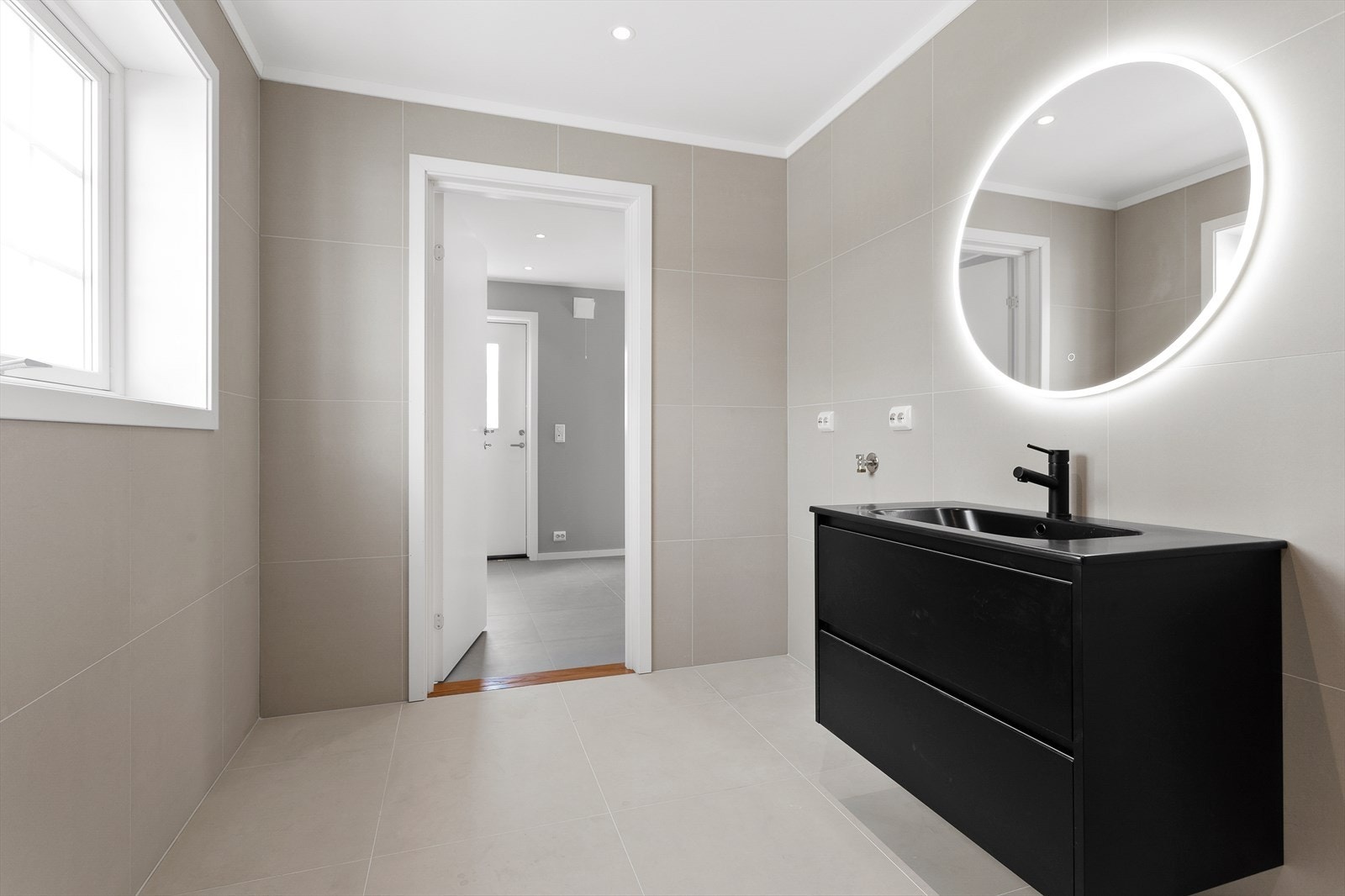 Baderomsinnredningen fra Alterna består av servant med sorte skuffer og et rundt speil med integrert belysning. Sorte detaljer gir et stilrent og gjennomført uttrykk. Galleribilde