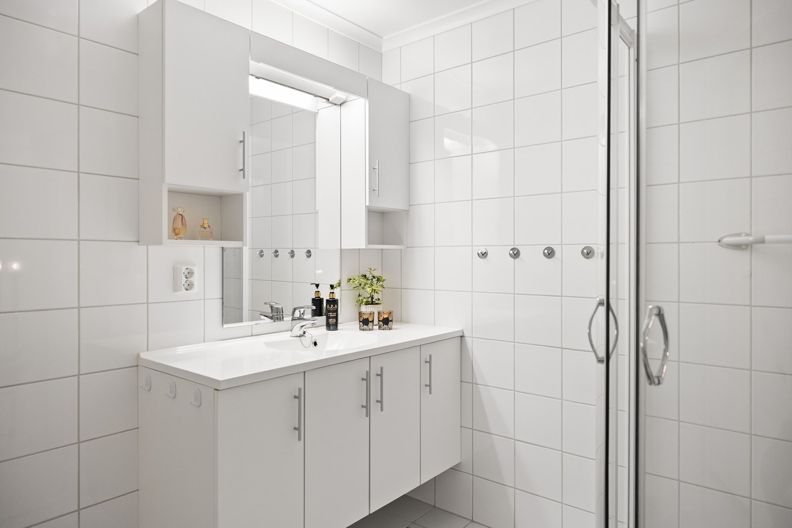 Taket har malte plater som gir rommet en lys og ren avslutning, og bidrar til en helhetlig og velholdt fremtoning. Innredningen består av et praktisk dusjhjørne, servantskap med tilhørende speil samt to overskap som gir gode oppbevaringsmuligheter. Galleribilde