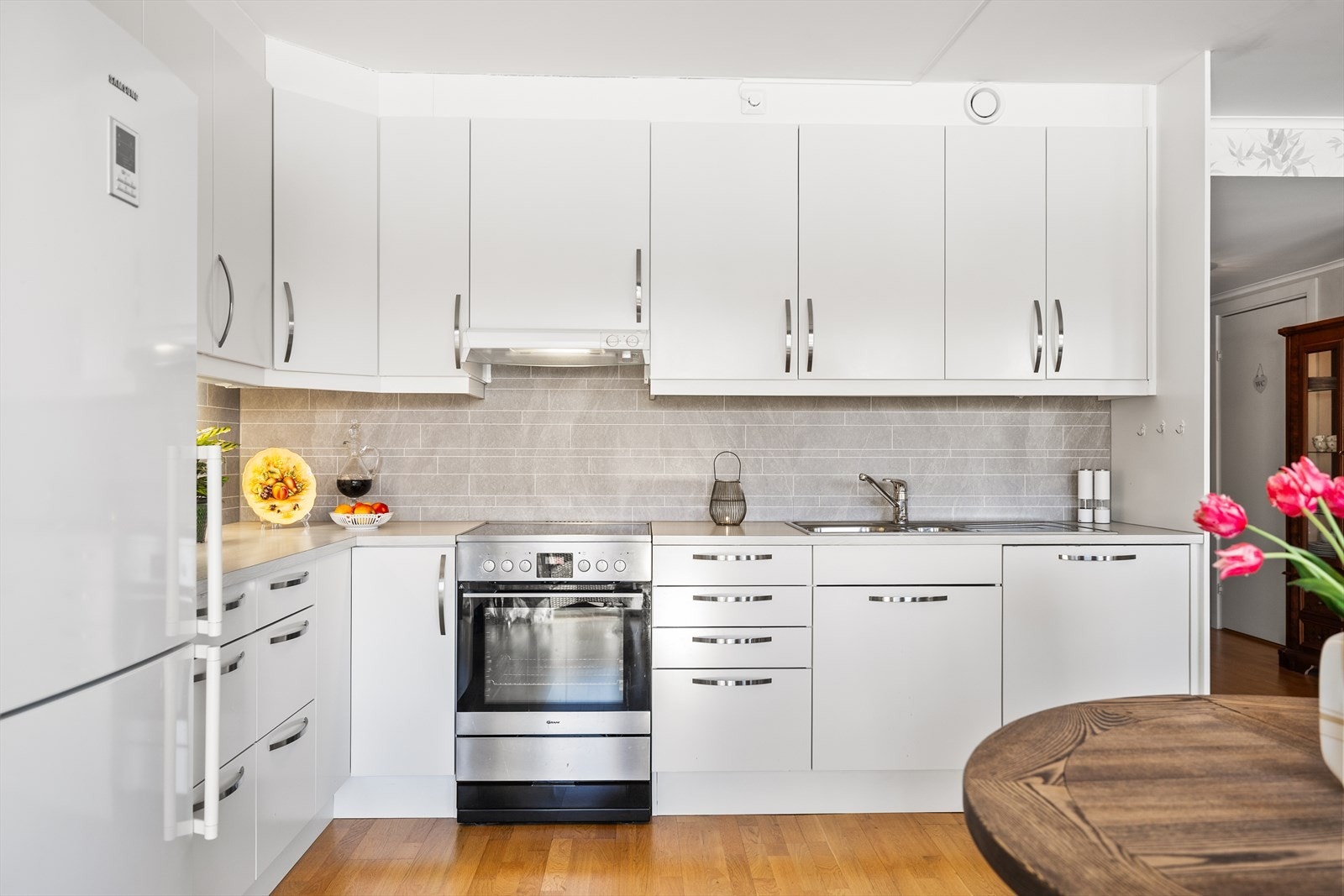 Kjøkkenet fremstår som stilrent og praktisk, med innredning i glatte fronter som gir et moderne og ryddig uttrykk. De slette flatene skaper en tidløs estetikk og er samtidig enkle å holde rene - perfekt for en effektiv hverdag. Galleribilde