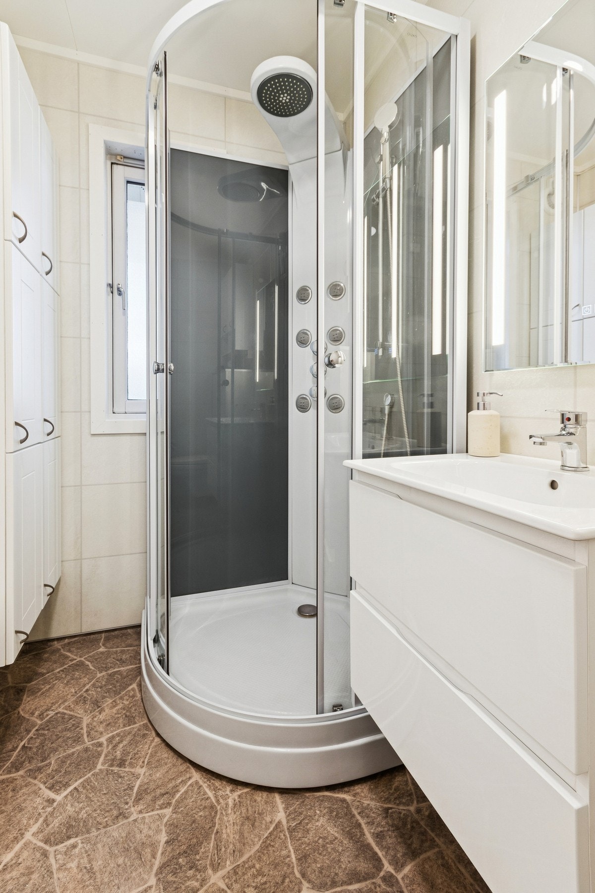 Rommet er innredet med nedfelt servant, veggmontert toalett, dusjkabinett og elektrisk styrt vifte. Galleribilde