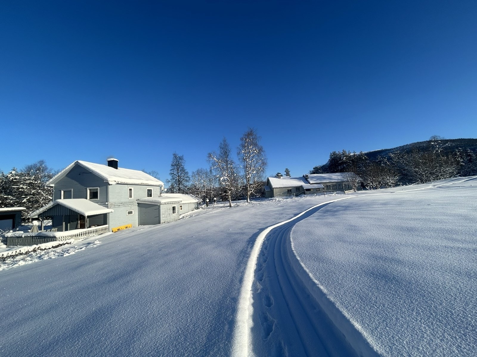 En solrik og landlig eiendom bebygd med stor enebolig og et eldre rødt anneks på 14m². Boligen har integrert garasje, bod og verksted. (selgers private bilde) Galleribilde