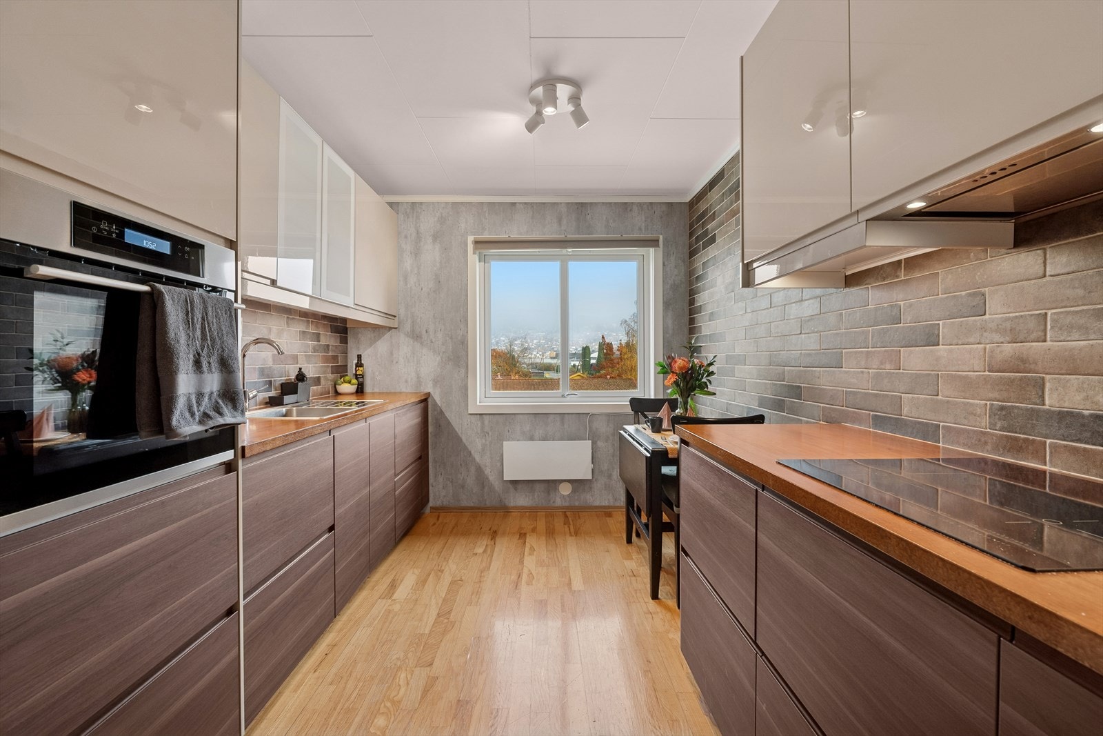 IKEA kjøkkeninnredning fra 2018 med glatte fronter. Det er enkelte glassfronter på overskapene og sprutbeskyttelse på vegg i form av fliser. Galleribilde