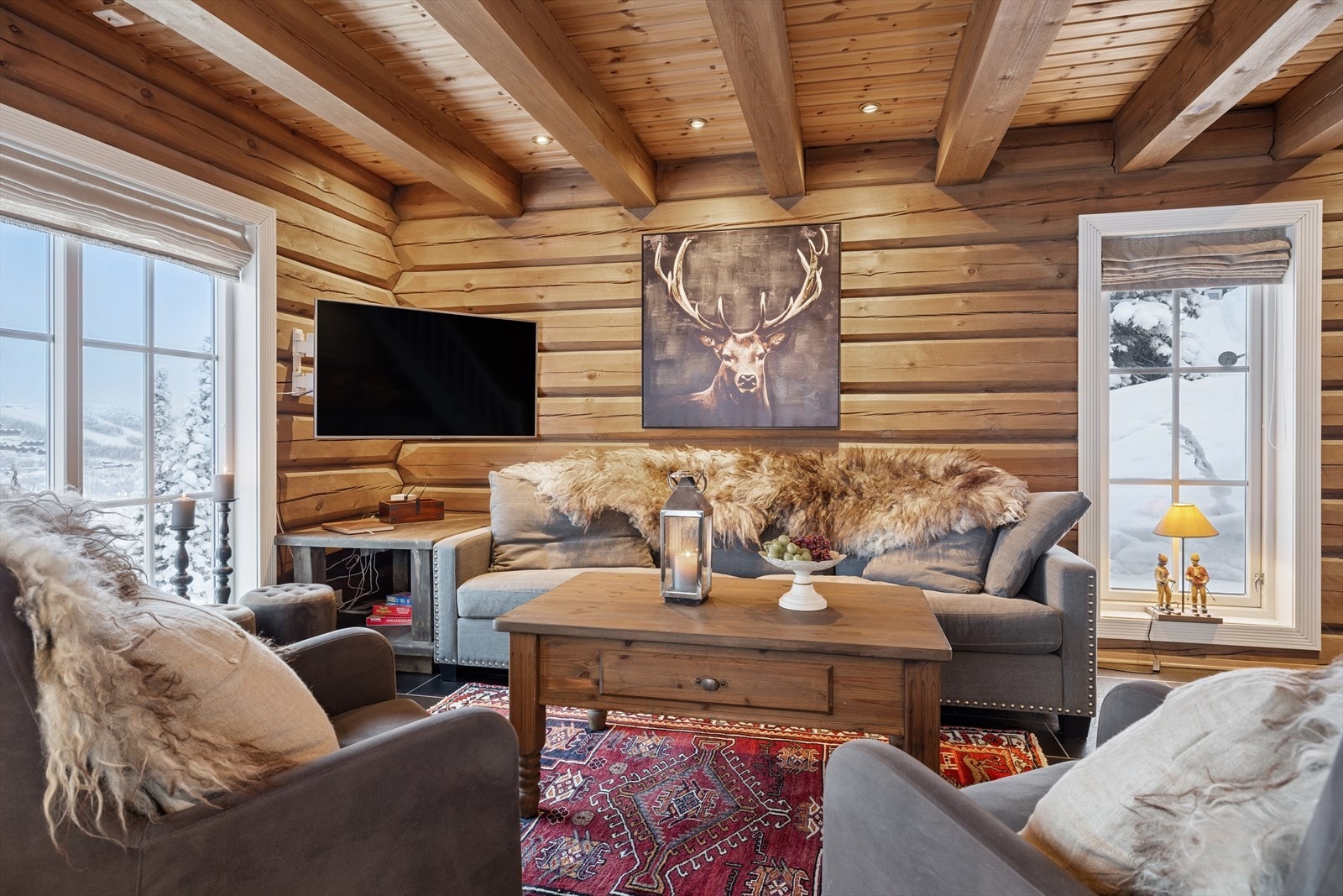 Det mørke, elegante flisgulvet fra entréen videreføres sømløst inn i stuen, og den gode takhøyden kombinert med de klassiske tømmerveggene skaper en varm og eksklusiv fjellhyttefølelse Galleribilde