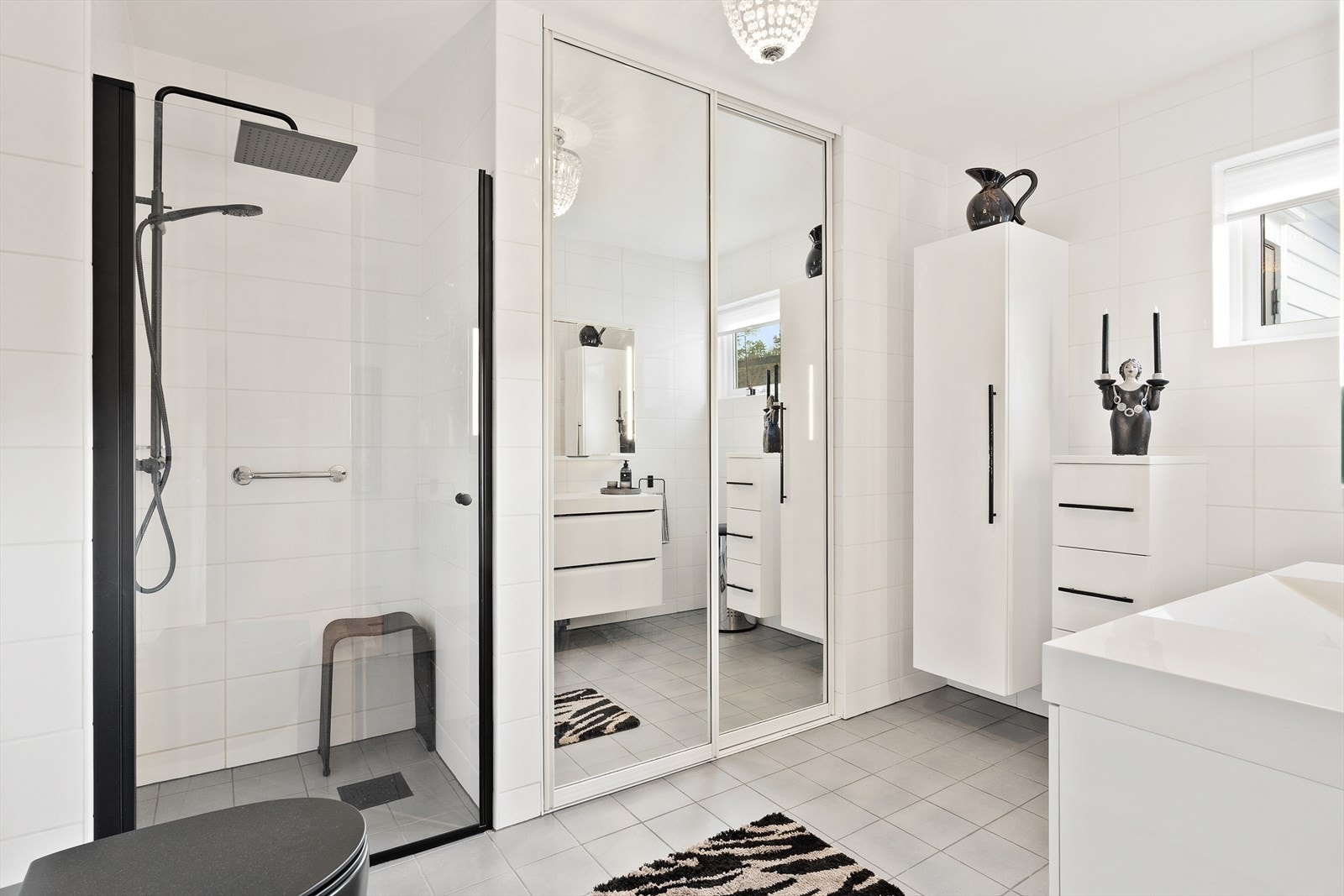 Badet er utstyrt med innredning som inkluderer nedfelt servant, veggmontert toalett, dusjvegger/-hjørne og opplegg for vaskemaskin Galleribilde