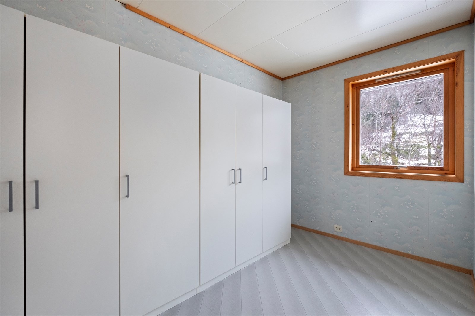 Garderobeløsning med hvite skap gir effektiv oppbevaring i soverommet. Store vinduer slipper inn naturlig lys og gir utsikt mot hageområdet. Galleribilde