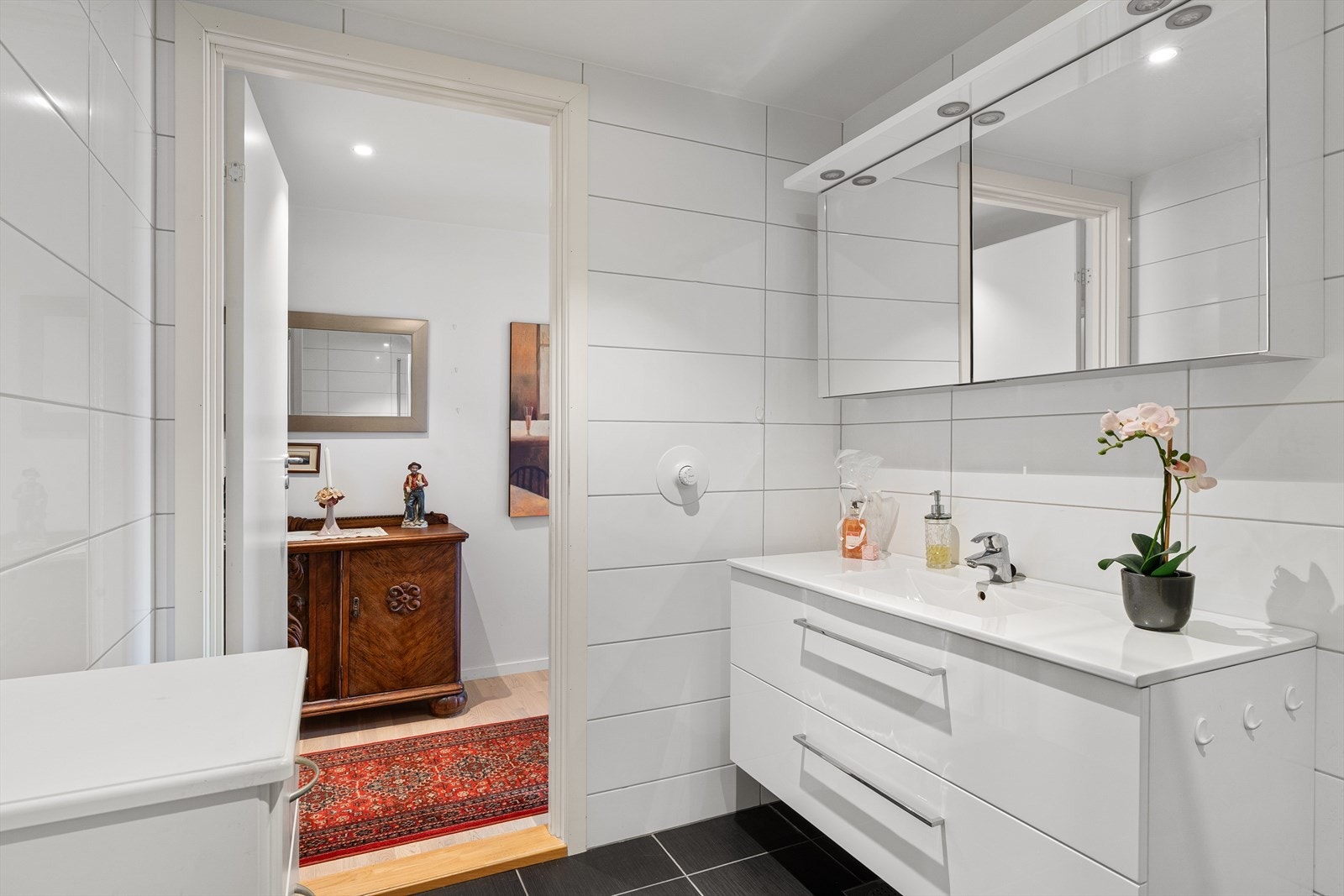 Helfliset baderom med vannbåren gulvvarme, dusjhjørne, vegghengt toalett og servant i skuffeinnredning. Galleribilde