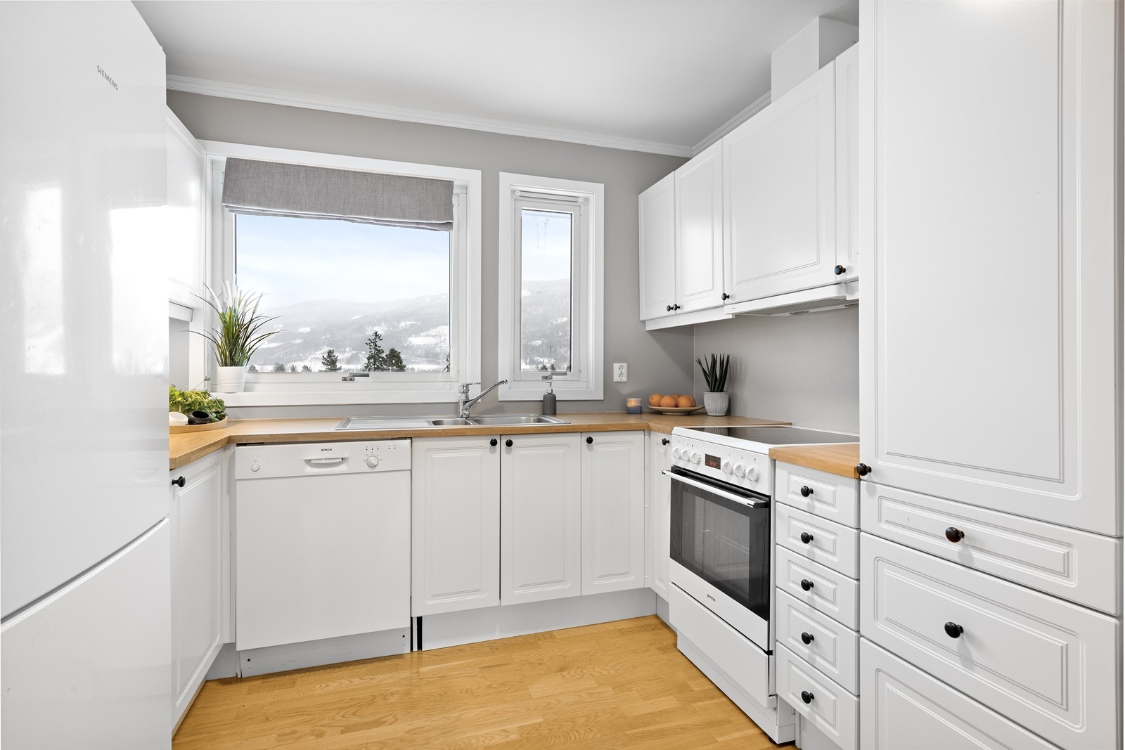 Kjøkkenet består av innredning med profilerte fronter og en benkeplate i laminat, samt avsatt plass til hvitevarer. Galleribilde