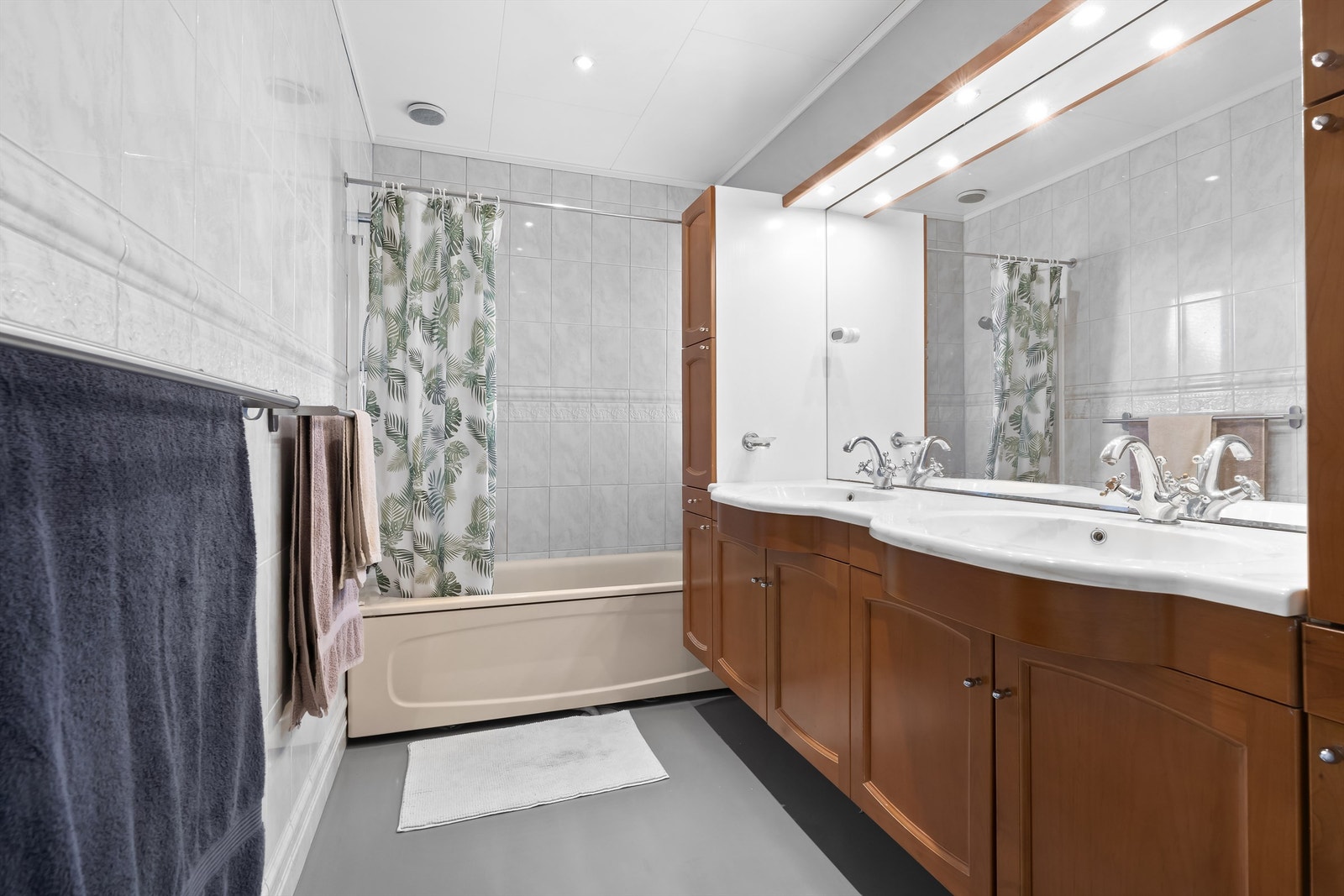 Stor baderom med badekar, dusj og stor servant og speil med god belysning og tilhørende store oppbevaringsskap. Galleribilde