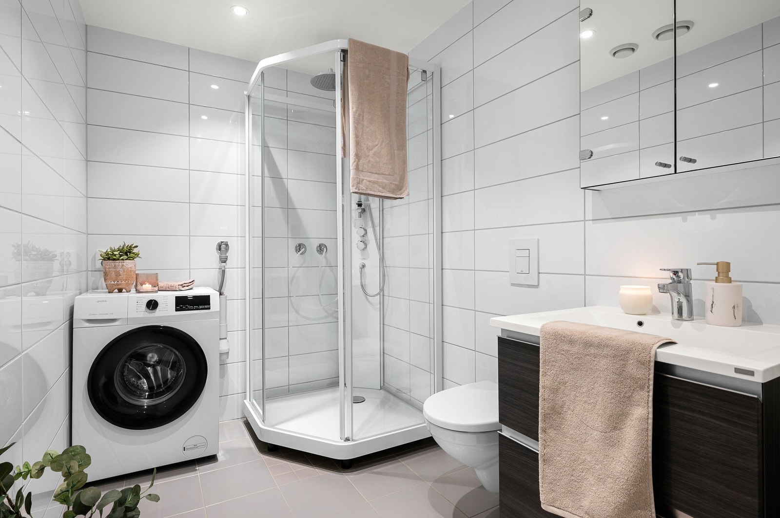 Boligens bad har dusjkabinett, toalett, opplegg for vaskemaskin, servant og speil med skap. Galleribilde