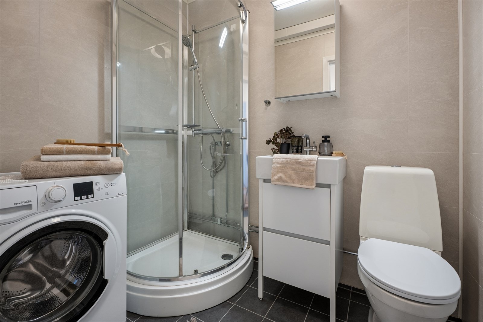 Rommet er innredet med et dusjkabinett, servant med tilhørende skap og et toalett. Det er også opplegg for vaskemaskin. Galleribilde