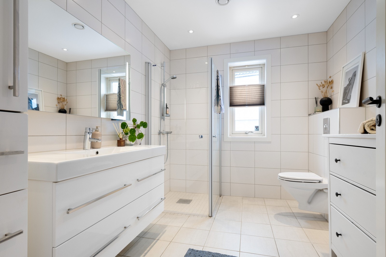 Badet er pent flislagt og har varmekabler i gulv. Rommet er innredet med dusjnisje med innfellbare glassdører, toalett og servantinnredning med speil. Galleribilde