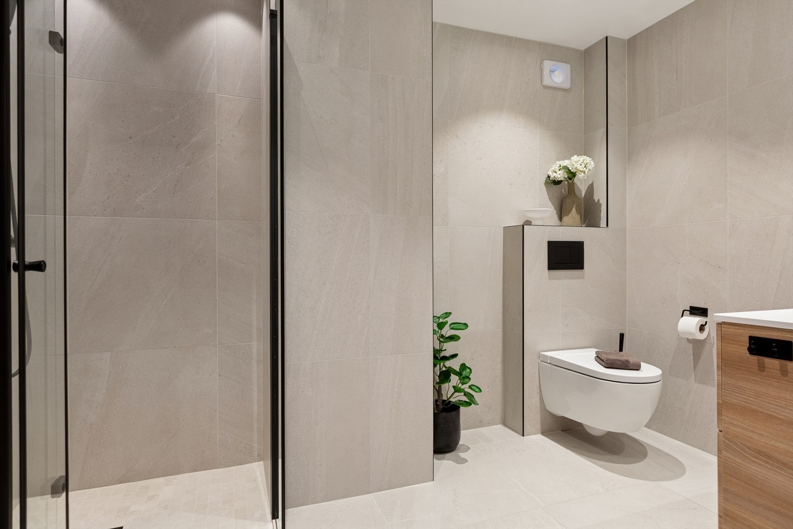 Badet er innredet med vegghengt toalett, dusjnisje med glassvegg, veggskap og baderomsinnredning med servant og blandebatteri. Galleribilde