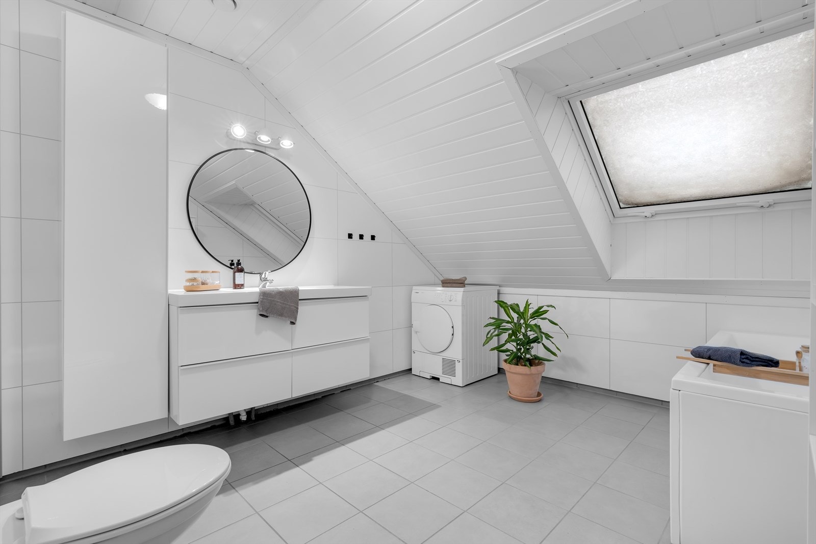 Badet i 2. etasje er svært romslig og preget av en lys og innbydende atmosfære. Flislagt gulv med varmekabler gir en behagelig følelse under føttene, og et stort Velux-vindu slipper inn rikelig med naturlig lys. Galleribilde