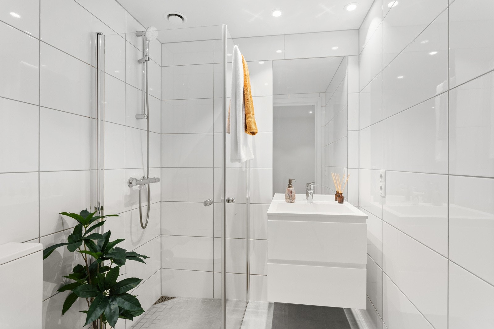 Baderom med adkomst fra entré/gang har vegghengt servantinnredning med skuffer, speil, dusjhjørne med innfellbare glassdører og gulvstående toalett. Galleribilde