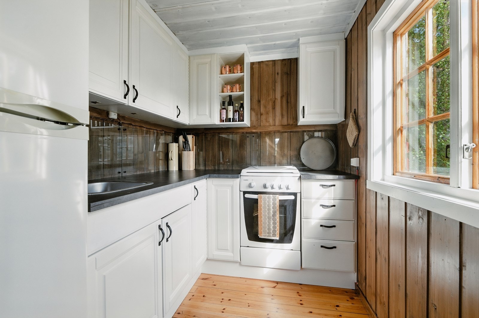 Kjøkkenet har en pen, takhøy innredning med profilerte fronter, laminat benkeplate og beskyttelsesplater over kjøkkenbenk. Det er avsatt plass til kjøleskap og komfyr. Galleribilde