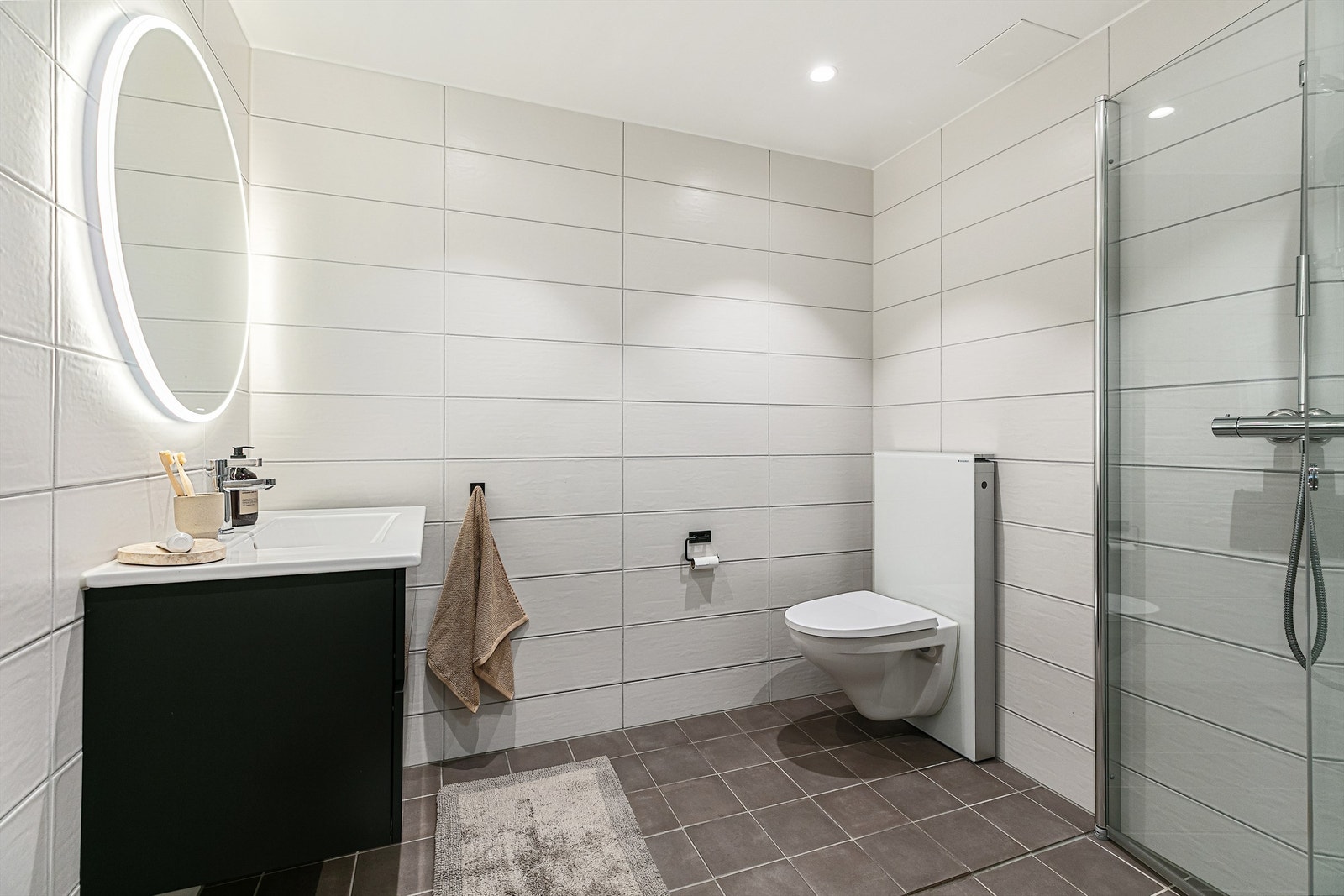 Baderommet består av flislagt gulv med gulvvarme og flislagte vegger, dusjhjørne med innfellbare glassdører og vegghengt servant. Galleribilde